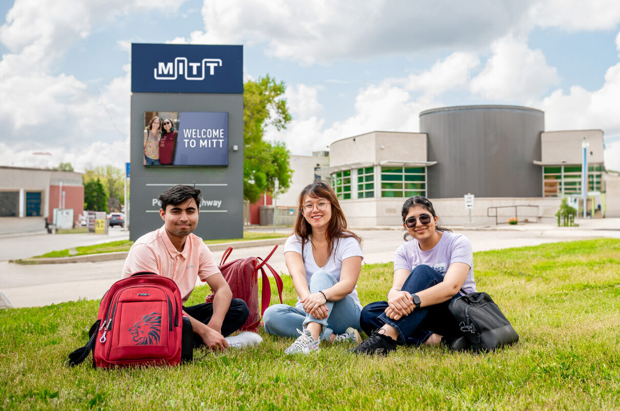 students sitting on campus lawn in front of campus sign