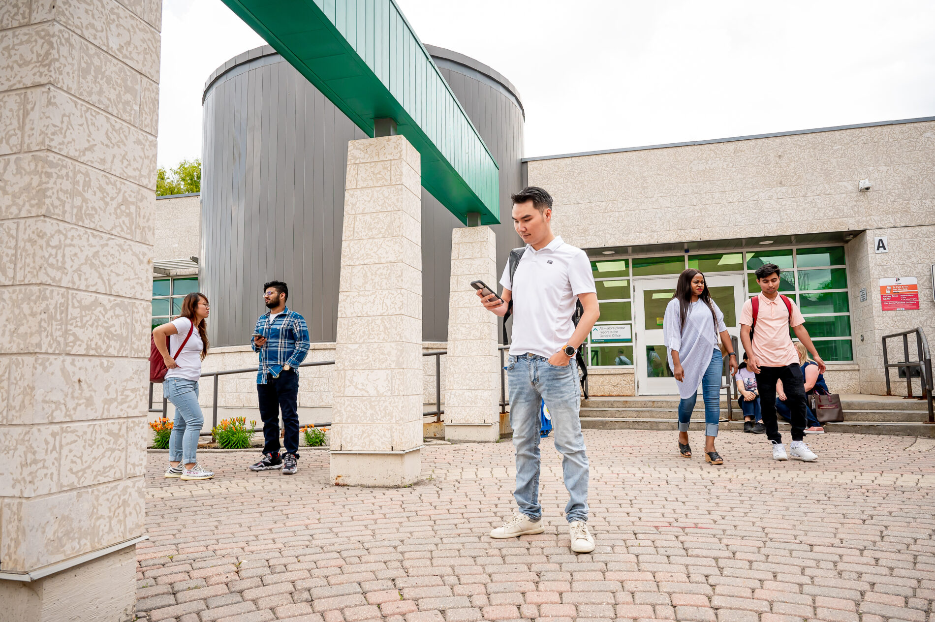 student looking at his phone in front of campus building. Students walking in front of campus building.