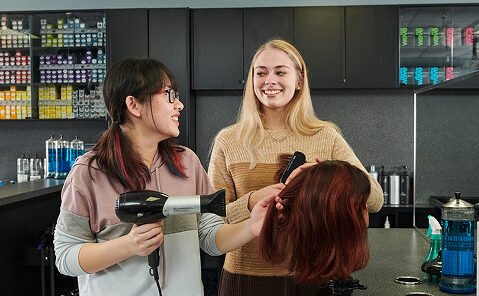 Students blow-drying a wig