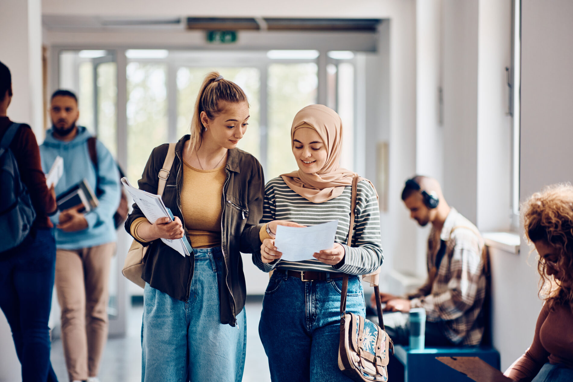 Female students going through lecture notes while walking through the hallway.