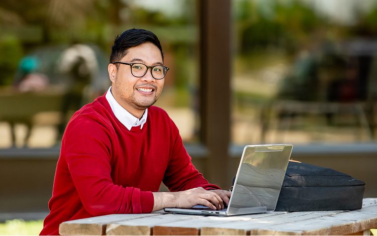 Smiling student outside on a laptop